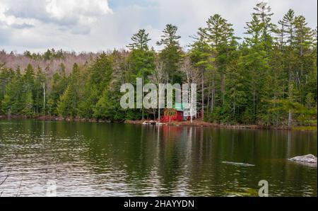 Une cabane rouge au bord d'un lac de montagne, dans une forêt de feuillus d'épinette-sapin-nord. Kettle Pond State Park, Groton, Vermont Banque D'Images