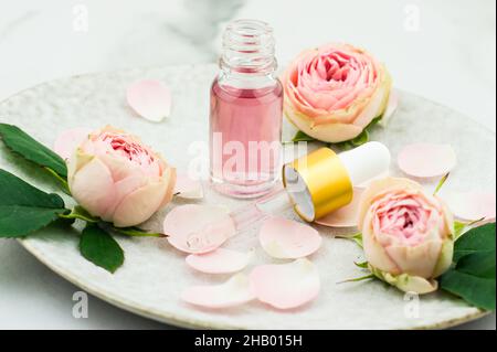 une bouteille ouverte d'huile de rose et une pipette remplie de cosmétiques pour le rajeunissement et le soin du visage sur une plaque en céramique Banque D'Images