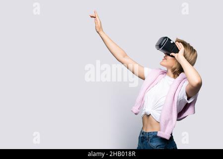 Vue latérale d'une femme jouant à un jeu avec un périphérique VR, pointant vers un espace de copie isolé sur fond blanc Banque D'Images