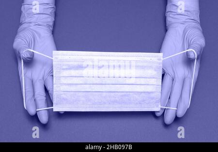 Mains dans des gants médicaux tient le masque sur fond lilas.Masque médical respiratoire de protection contre la propagation du virus.Gros plan, espace de copie Banque D'Images