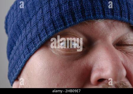 Regarde-moi dans l'œil.Gros plan sur l'œil marron d'un homme.Un homme cultivé dans un chapeau bleu grimaces. Banque D'Images