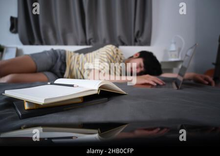 Un homme asiatique fatigué dorment sur le lit avec des livres la nuit. Banque D'Images