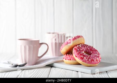 Beignets à la glaçure rose et à la poudre de caramel colorée sur fond blanc en bois. Banque D'Images