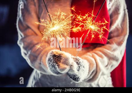 Filles mains tenant le sparkler brûlant dans des gants neigeux pull tricoté et foulard rouge. Banque D'Images