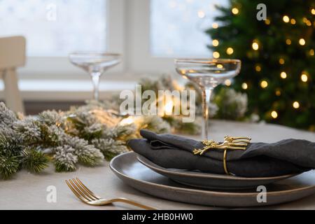 Table de Noël avec des assiettes grises vides élégantes décorées de ronds de serviettes dorées près de l'arbre de Noël.Dîner de vacances en famille à la maison.Gros plan. Banque D'Images