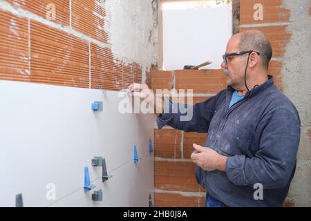 Travailleur senior du constructeur en ajustant la séparation entre les carreaux sur le mur. Banque D'Images