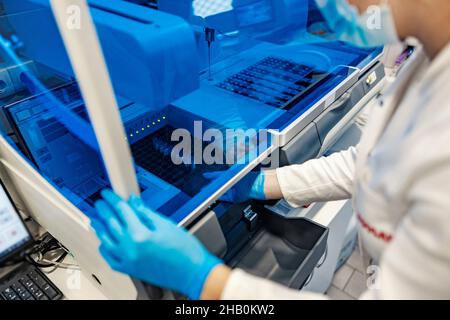 Microbiologie et technologie moderne en laboratoire.Un scientifique avec des gants stériles se trouve à côté d'une machine pour l'analyse de sang et la mise de tubes à essai wi Banque D'Images