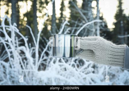 La main dans la mitaine tient la tasse en métal dans la forêt Banque D'Images