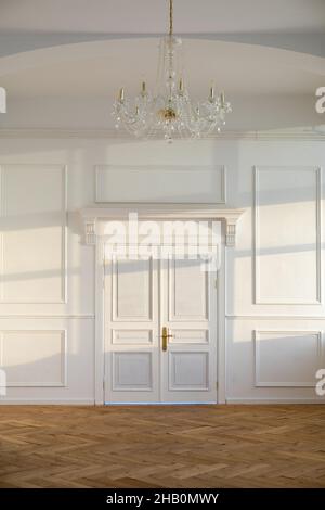 Portes fermées blanches dans une pièce claire et spacieuse au design classique et lustre suspendu au plafond près du mur avec lumière du soleil Banque D'Images
