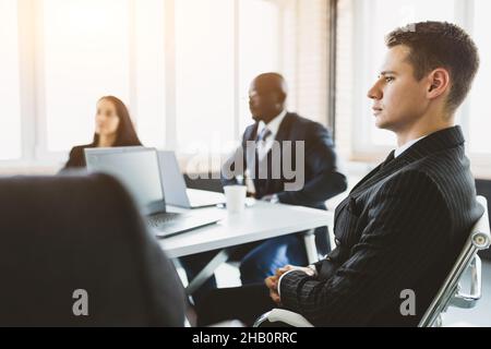 Les jeunes gens d'affaires travaillent et communiquent lorsqu'ils sont assis au bureau avec leurs collègues. Réunion d'affaires Banque D'Images