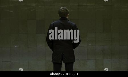 Jeune homme solitaire de derrière à la station de métro.Un jeune homme attend un train dans le métro, vue arrière. Banque D'Images