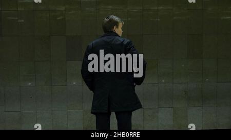 Jeune homme solitaire de derrière à la station de métro.Un jeune homme attend un train dans le métro, vue arrière. Banque D'Images