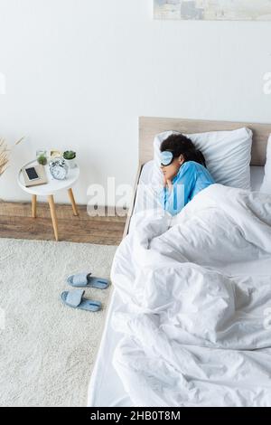 vue en grand angle de la femme afro-américaine dans un masque oculaire dormant au lit Banque D'Images