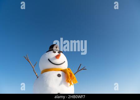 Bonhomme de neige drôle dans un élégant chapeau marron et jaune scalf sur un terrain enneigé. Ciel bleu sur fond Banque D'Images