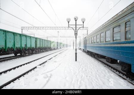 Gare de peron couverte de neige en hiver.Trains de voyageurs et wagons de marchandises sur des chemins de fer enneigés.Ukraine, Europe Banque D'Images