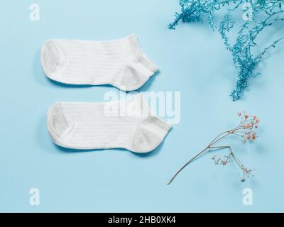 Paire de chaussettes blanches pour femmes et branches décoratives sur fond bleu, vue du dessus. Banque D'Images