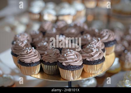 Cupcakes au chocolat avec glaçage au chocolat et srinkles de perles dans des cuos en papier doré Banque D'Images