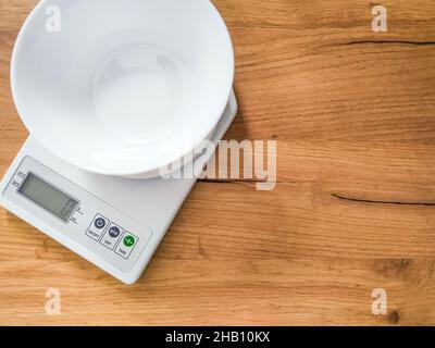 Balance de cuisine moderne électronique numérique avec bol vide sur table en bois. Banque D'Images