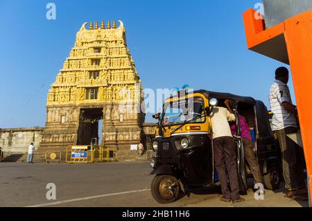 Belur, Karnataka, Inde : Un groupe d'hommes se trouve près d'un pousse-pousse automatique, à côté de la porte gopuram du temple de Cheannakhava. Banque D'Images