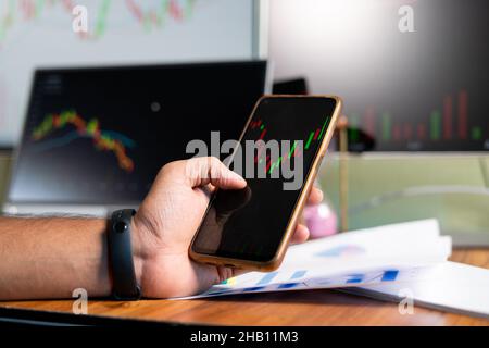 Gros plan des mains de Trader regardant les graphiques boursiers sur l'application de téléphone mobile - concept d'investir de l'argent sur des actions en utilisant l'analyse technique, le trading ou Banque D'Images