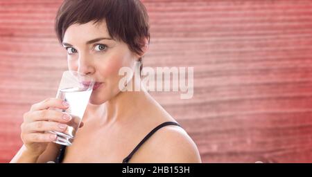 Image composite d'une femme du caucase buvant de l'eau à partir d'un verre sur fond texturé rose Banque D'Images