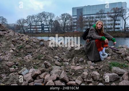 Berlin, Allemagne.Jeune adulte punk dude assis sur une pile de roche près d'un immense lieu de graffitis, un peu à Spandau. Banque D'Images