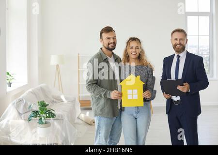 Portrait de l'agent immobilier masculin et du couple heureux qui viennent d'acheter leur première maison. Banque D'Images