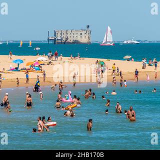 Île d'Oléron (au large des côtes de l'ouest de la France) : touristes sur la plage et dans l'eau en été avec fort Boyard au loin Banque D'Images