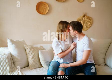 Jeune couple à la maison dans des vêtements décontractés.Guy et fille embrassent et embrasse, en s'amusant, aiment passer du temps ensemble, assis sur le canapé à la maison. Banque D'Images