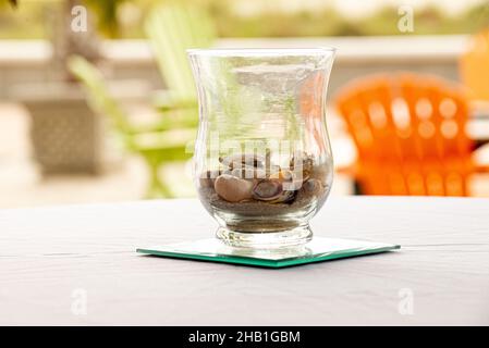 Vase en verre pièce maîtresse remplie de coquillages sur table blanche à l'extérieur près de la plage Banque D'Images