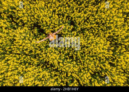 Femme en robe jaune au champ de colza en fleurs.Fleurs jaunes vives et femme heureuse Banque D'Images