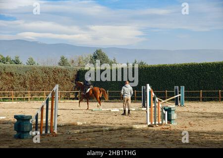 Enfant apprenant l'équitation avec des obstacles au ranch avec un entraîneur. Banque D'Images