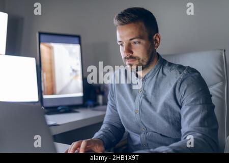 Jeune sérieux caucasien beau architecte barbu assis au bureau tard dans la nuit et finissant le projet. Banque D'Images