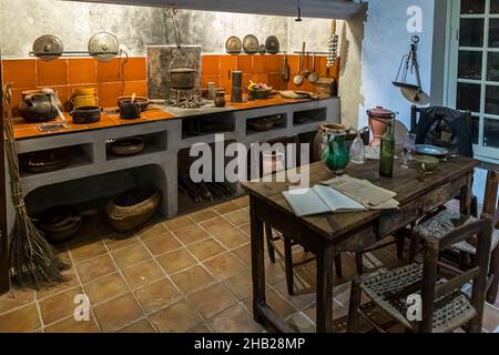 Une cuisine provençale reconstituée avec une cheminée ouverte, des casseroles en cuivre et des cruches en faïence est exposée au Musée des Arts et Traditions Populaires à Draguignan, dans le département du Var, en France ; un vieux livre ouvert repose sur la table en bois devant elle. Banque D'Images