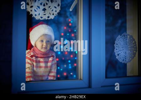 L'enfant regarde par la fenêtre et attend le Père Noël pour Noël ou le nouvel an Banque D'Images