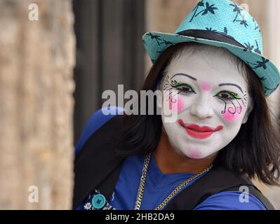 Un jeune clown mexicain avec un maquillage de clown blanc fait des peks autour du coin du mur le jour des morts (Día de los Muertos) et regarde le spectateur. Banque D'Images