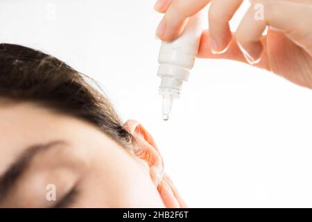 Traitement des maladies de l'oreille.Une femme burie tombe dans son oreille, gros plan.Isolé sur un fond blanc.Copier l'espace.Le concept de santé auditive et de Banque D'Images