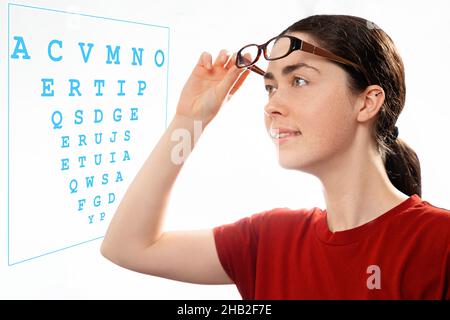 Ophtalmologie.Portrait d'une jeune belle femme qui prend ses lunettes et regarde un diagramme pour vérifier sa vision.Le concept de la santé des yeux an Banque D'Images