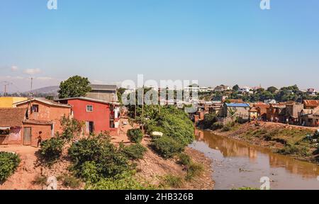 Antananarivo, Madagascar - 07 mai 2019: Le soleil brille sur des maisons simples près de la petite rivière boueuse, peu de gens malgaches marchant, paysage typique de la banlieue Banque D'Images