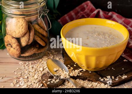 Vue hachée sur un bol de lait et de flocons d'avoine et un pot de petits gâteaux aux raisins secs. Banque D'Images
