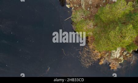 Magnifique paysage scandinave photographié avec un drone lors d'une journée ensoleillée de fin d'automne ou d'hiver.Île avec arbres à feuilles persistantes dans le lac gelé. Banque D'Images