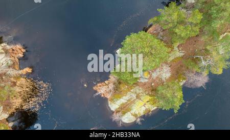 Magnifique paysage scandinave photographié avec un drone lors d'une journée ensoleillée de fin d'automne ou d'hiver.Île avec arbres à feuilles persistantes dans le lac gelé. Banque D'Images