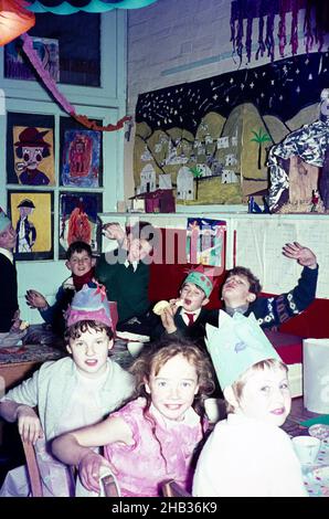 Fête de Noël dans la salle de classe primaire enfants portant des chapeaux et manger tirant des visages drôles, Royaume-Uni, c 1960 Banque D'Images