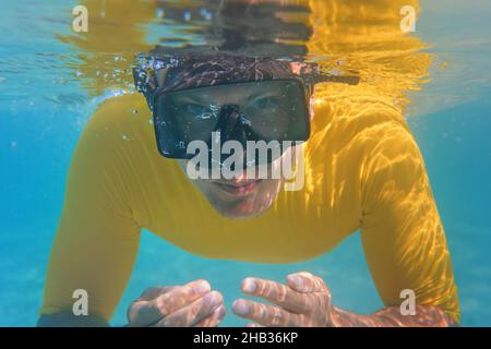 Jeune homme en chemise jaune nageant sous le visage de l'eau recouvert d'un masque de plongée ou de plongée avec tuba, gros plan sur le devant Banque D'Images