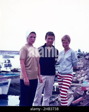 Un homme et deux femmes vêtus de façon tendance à côté des bateaux en vacances en Espagne, 1966 Banque D'Images
