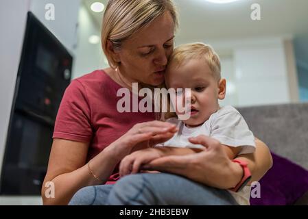 le petit garçon est triste sur les genoux de maman, sa main fait mal. Banque D'Images