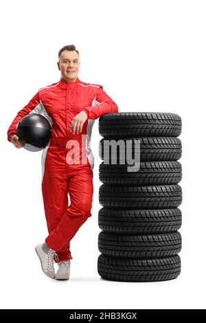 Portrait complet d'un coureur en costume rouge, appuyé sur un tas de pneus et tenant un casque isolé sur fond blanc Banque D'Images