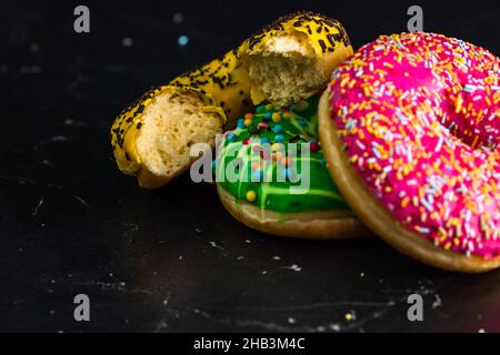 Gros plan d'un donut vitrifié avec deux beignets colorés isolés sur un fond noir Banque D'Images