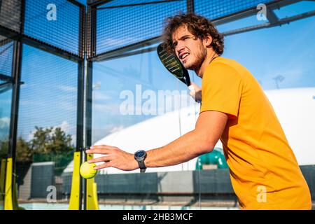 Un padel ou un joueur de tennis se prépare à servir une balle de tennis pendant un match - le formateur enseigne au garçon comment jouer au padel sur un court de tennis extérieur