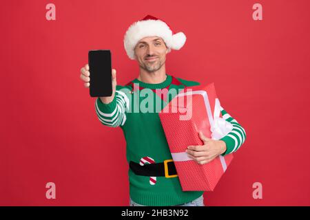 joyeux homme elf dans le chapeau du père noël présentant smartphone. publicité de noël. Banque D'Images